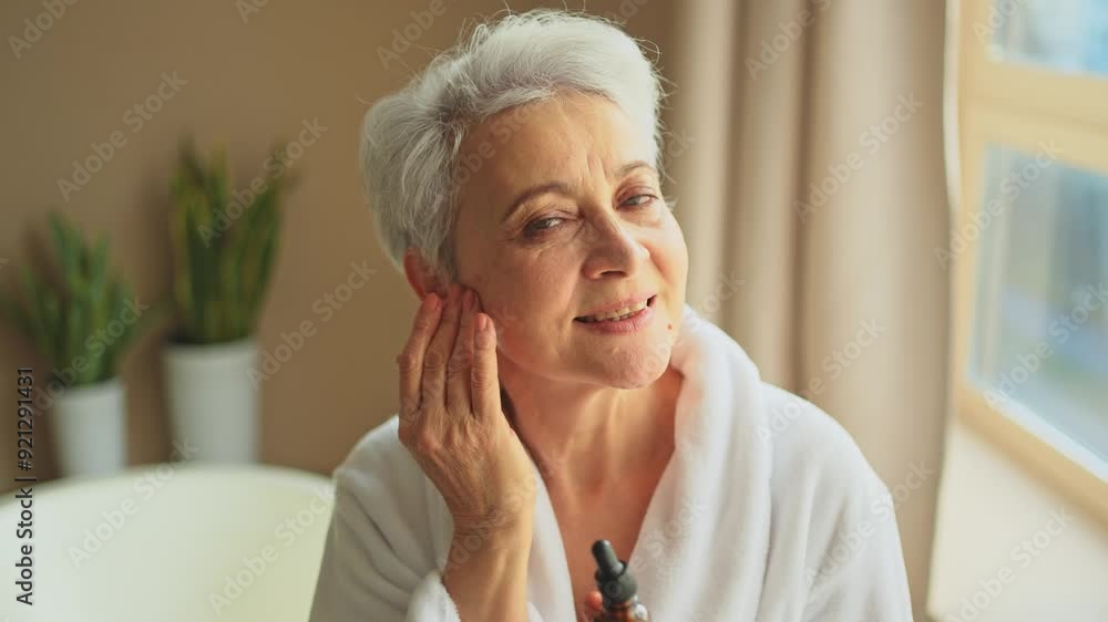 Woman applying natural drops cosmetics oil to face skin. Mature adult old woman applying nourishing anti age serum with pipette doing daily beauty routine. Senior woman gets kin scare facial treatment Woman applying natural drops cosmetics oil to face skin. Mature adult old woman applying nourishing anti age serum with pipette doing daily beauty routine. Senior woman gets kin scare facial treatment