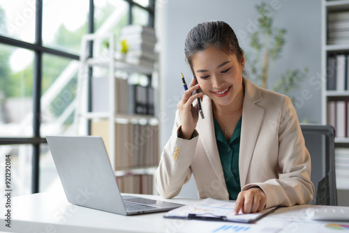 Businesswoman is working in her bright modern office, analyzing charts and talking on the phone