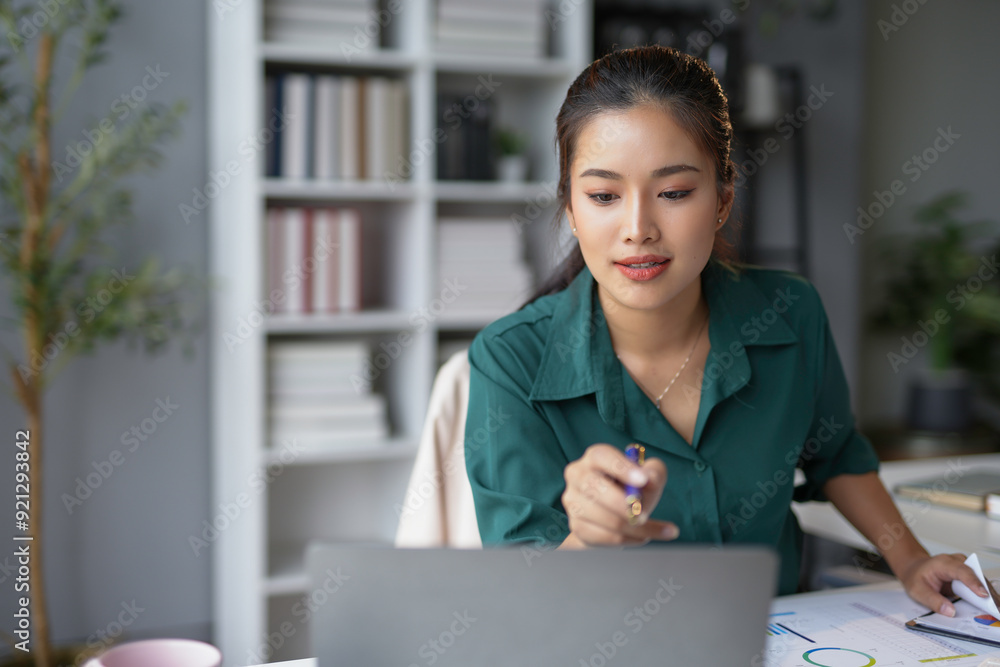 Young businesswoman is working from home, analyzing charts on her laptop and taking notes Young businesswoman is working from home, analyzing charts on her laptop and taking notes