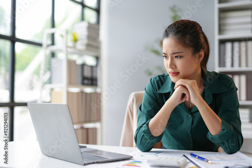 Картината върху платно Young asian businesswoman is frowning and looking worried while working on a lap