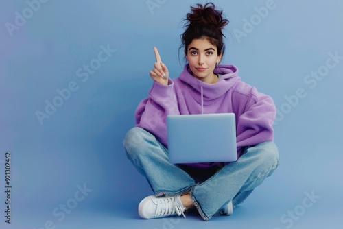 Full body photo girl sit floor legs crossed work laptop point index finger copyspace direct way follow comment ads wear lilac violet pullover denim jeans isolated blue color background