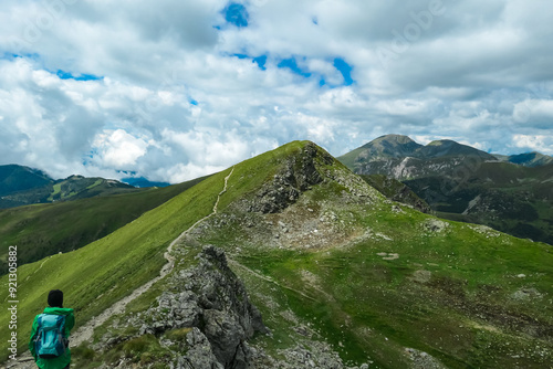 Hiker woman with scenic hiking trail to Klomnock along lush green alpine meadows in biosphere park Nock mountains, Gurktal Alps, Carinthia, Austria. Rolling gentle hills. Wanderlust in Austrian Alps