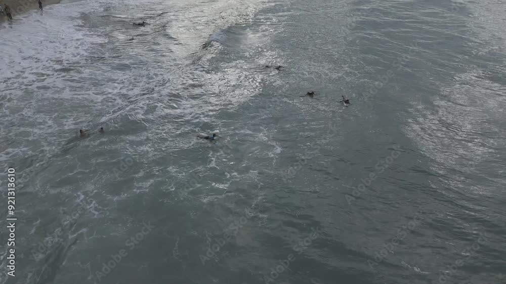 Drone hovers over surfers laying on boards as waves slowly rock under them Drone hovers over surfers laying on boards as waves slowly rock under them