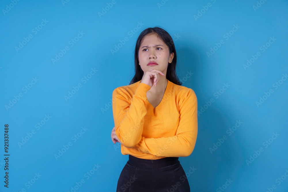Young woman in a thoughtful pose, hand on chin, against a blue background. Perfect for business, education, or professional themes Young woman in a thoughtful pose, hand on chin, against a blue background. Perfect for business, education, or professional themes
