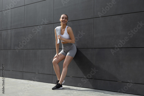 Pretty slim young woman in sportswear standing near the wall and looking relaxed