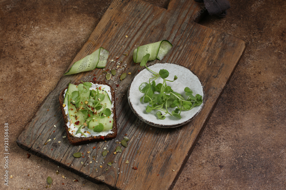 Rye bread with cucumbers, microgreens and cream cheese on a wooden board on a brown background. Rye bread with cucumbers, microgreens and cream cheese on a wooden board on a brown background.