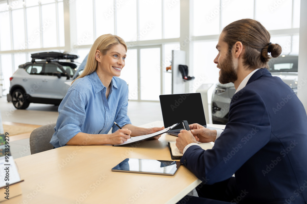 Woman buying new automobile completes purchase with male seller in car showroom Woman buying new automobile completes purchase with male seller in car showroom
