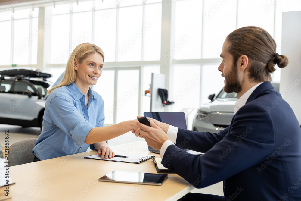 Fototapeta premium Woman buying new automobile completes purchase with male seller in car showroom