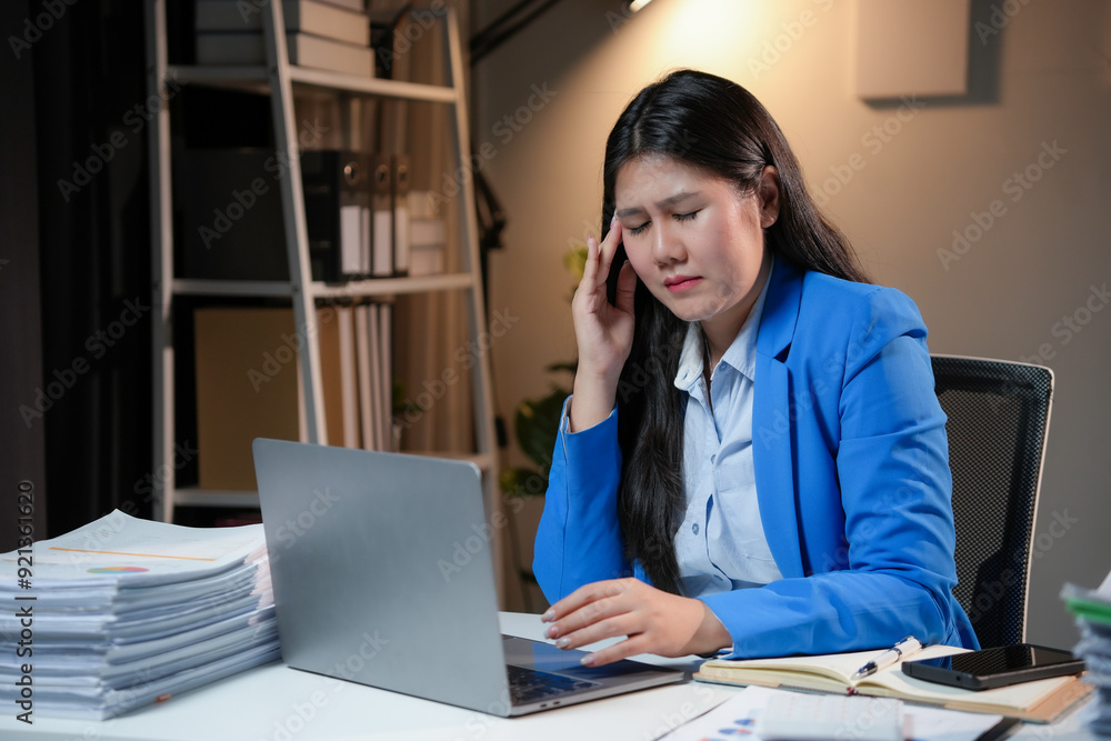 Businesswoman is feeling tired and having a headache while working on a laptop at her desk in the office Businesswoman is feeling tired and having a headache while working on a laptop at her desk in the office