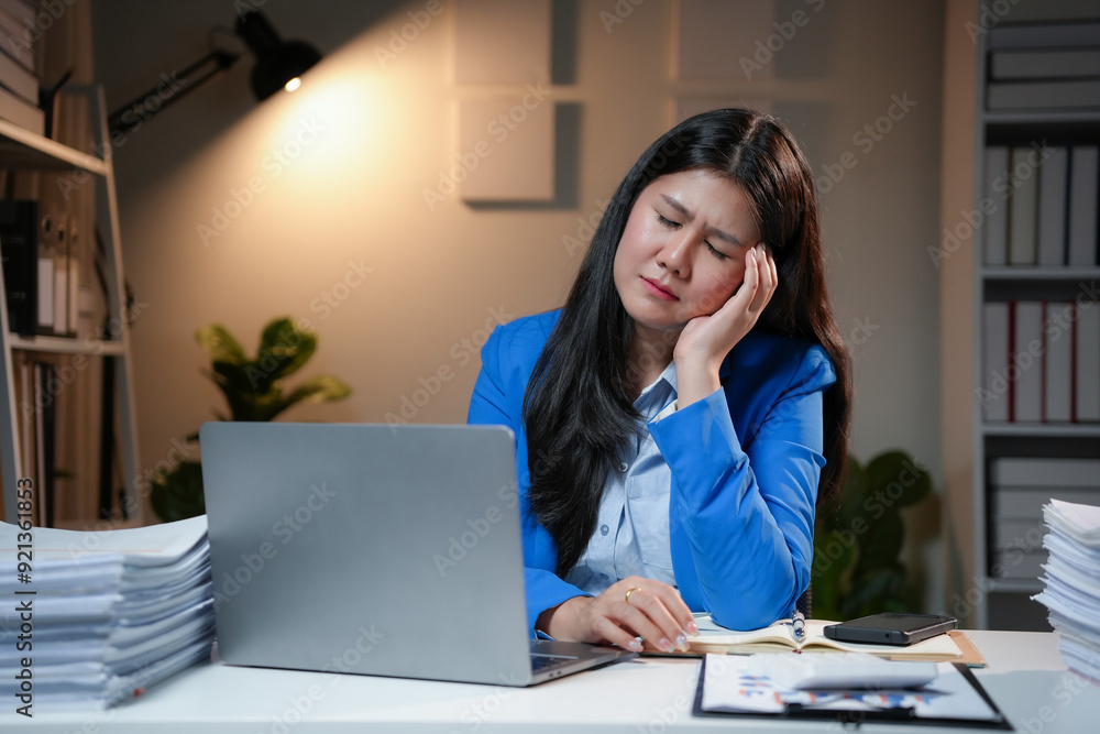 Stressed asian businesswoman having a headache while working late at night in an office with a laptop computer Stressed asian businesswoman having a headache while working late at night in an office with a laptop computer