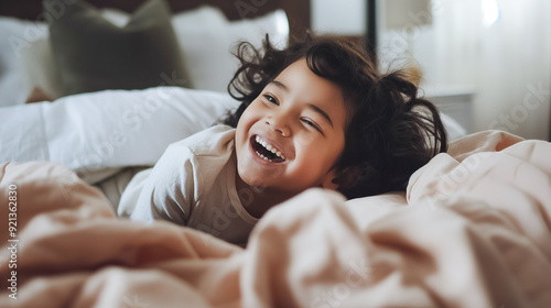 Adorable, joyful child is laughing happily while snuggled in their cozy bed, surrounded by soft blankets and a playful atmosphere