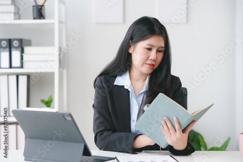 Asian businesswoman is sitting and reading notes in her notebook while working on a project at her desk