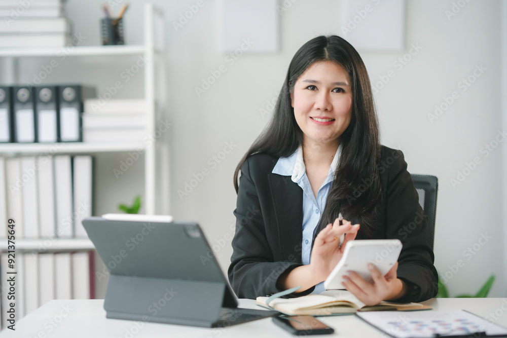 Smiling asian accountant woman calculating and analyzing financial data on digital tablet and financial chart at her office desk Smiling asian accountant woman calculating and analyzing financial data on digital tablet and financial chart at her office desk