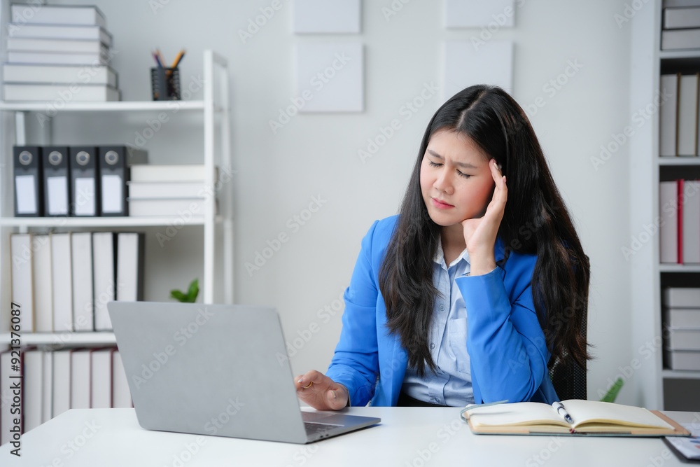 Stressed businesswoman holding her temples and feeling strong headache, working on laptop at office Stressed businesswoman holding her temples and feeling strong headache, working on laptop at office
