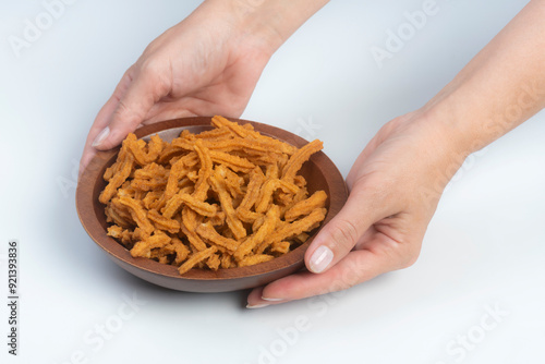 Studio shot of female hands holding a carved wooden bowl containing a heap of soy stick snakcs, isolated on white photo