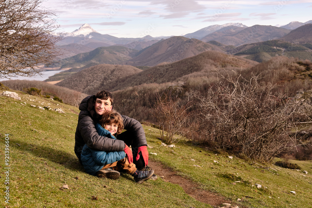 Fototapeta premium A portrait of two brothers sitting and embracing on the mountain.