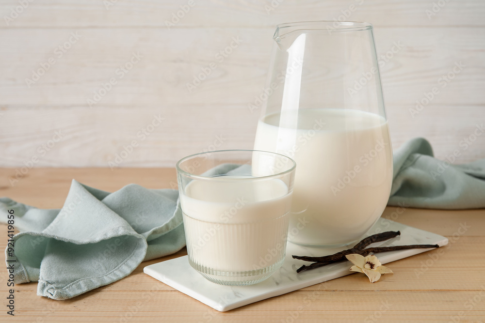 Glass and jug of fresh vanilla milk with sticks and flower on wooden table Glass and jug of fresh vanilla milk with sticks and flower on wooden table