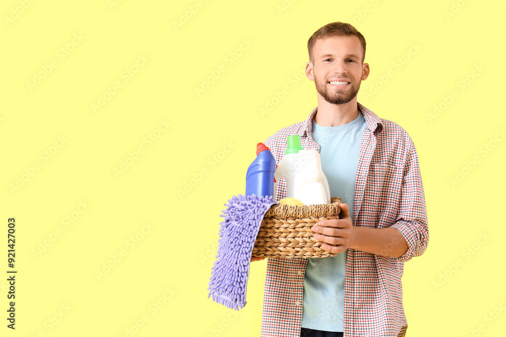 Male janitor holding basket with cleaning supplies on yellow background Male janitor holding basket with cleaning supplies on yellow background