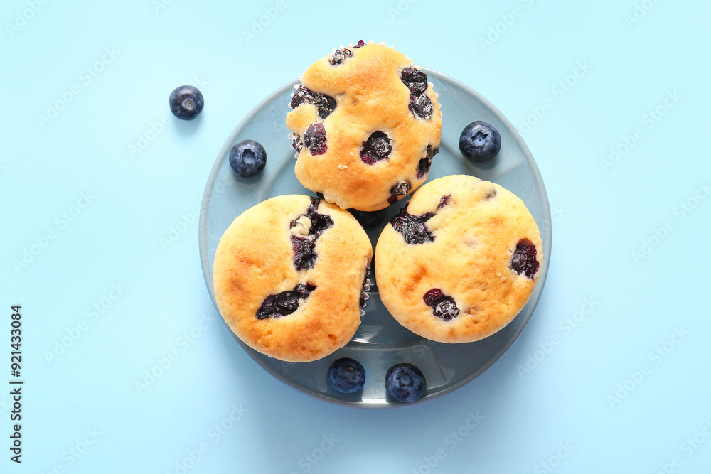 Plate with tasty blueberry muffins on blue background Plate with tasty blueberry muffins on blue background
