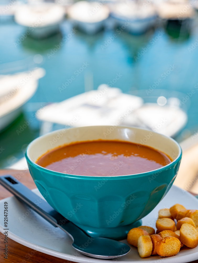 Homemade tasty fish or bisque soup with croutons and view on yacht boats and houses of Port Grimaud, French Riviera, France. Food of Provence Homemade tasty fish or bisque soup with croutons and view on yacht boats and houses of Port Grimaud, French Riviera, France. Food of Provence