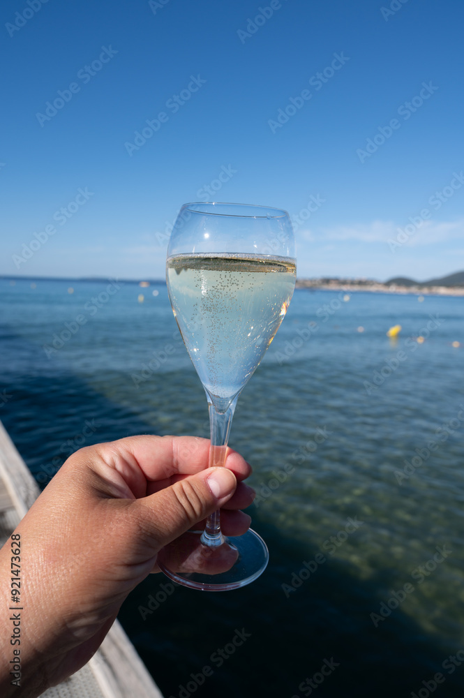 Obraz premium Summer time in Provence, hand with glass of cold champagne cremant sparkling wine on famous Pampelonne sandy beach near Saint-Tropez in sunny day, Var department, France, beach club party