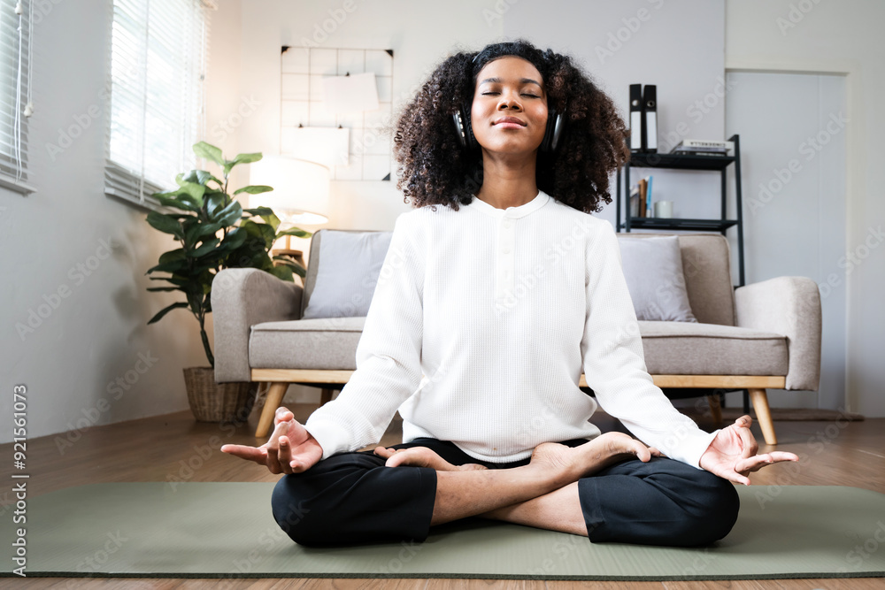 A black woman sitting in a yoga position in living room at home. A black woman sitting in a yoga position in living room at home.