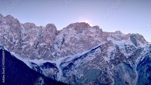 In the background a Vald di Scalve mountain rises majestically, its peak covered in a thick blanket of snow. The sun overlooks the slope, ready to warm up the adventure of mountaineers. photo