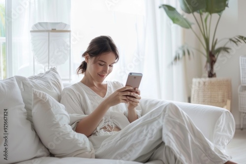 A young Caucasian woman checks her smartphone while sitting comfortably in a light-filled living room.