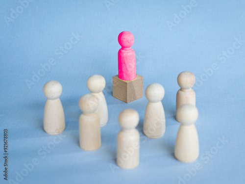 Red toy block standing on podium facing other toy blocks on desk. Illustrate leadership concept.