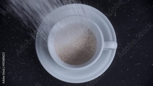 top view pouring sugar into white mug cup on black background