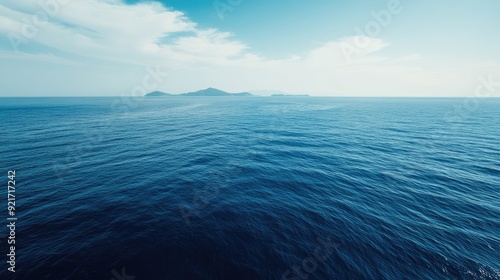 A top view of the deep blue ocean with a small island in the distance. Copy space on the left side.