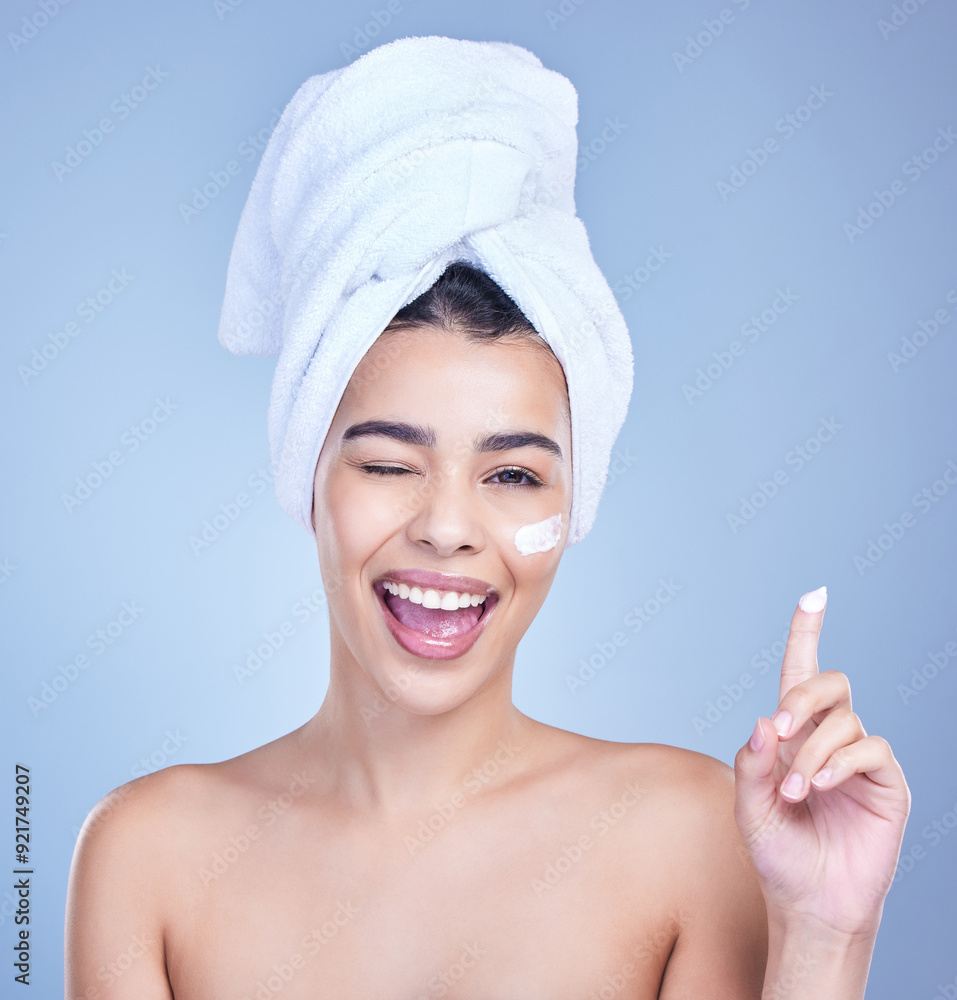 Studio, woman portrait and wink with cream for skincare, application and face wellness with cosmetics. Female model, beauty and treatment with lotion, moisturizer and results by blue background Studio, woman portrait and wink with cream for skincare, application and face wellness with cosmetics. Female model, beauty and treatment with lotion, moisturizer and results by blue background