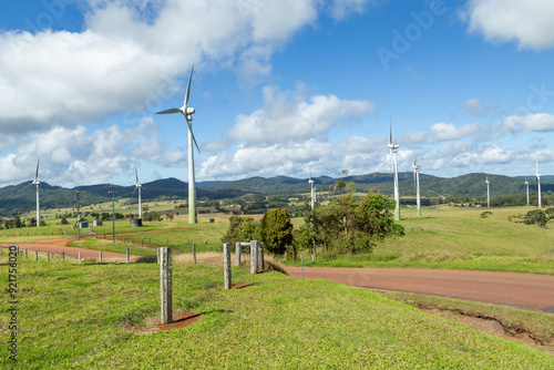 Wind turbines on a wind farm amongst the hills and grassy fields with fence posts in the foreground and a cloudy sky on the Atherton Tablelands on the road to Ravenshoe in Queensland, Australia.