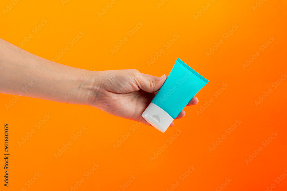 Blue cosmetic bottle, Skin care or sunscreen cosmetic in hand on orange background. Blue cosmetic bottle, Skin care or sunscreen cosmetic in hand on orange background.