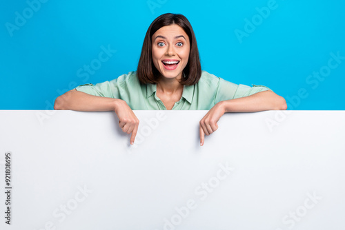 Photo of overjoyed woman dressed teal shirt indicating at awesome offer on billboard empty space isolated on blue color background