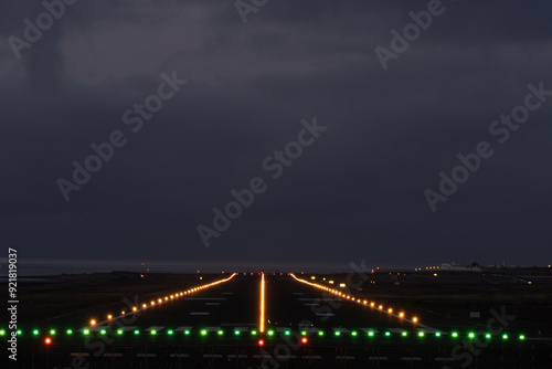 Empty airport runway at night, bathed in green and orange lights, guiding planes for safe takeoff and landing