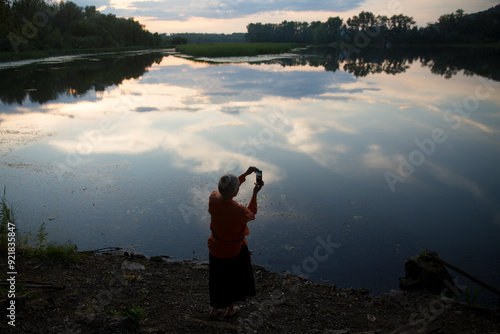 Wallpaper Mural portrait senior woman with gray hair takes a selfie with a mobile phone at sunset near the lake.  Enjoying the little things. spends time in nature in summer.   Torontodigital.ca