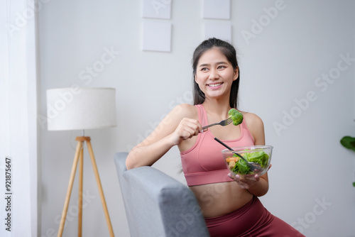 Young woman smiles happily as she enjoys a nutritious salad after working out at home, embodying a healthy lifestyle with clean eating and plant based nutrition, savoring each bite mindfully photo