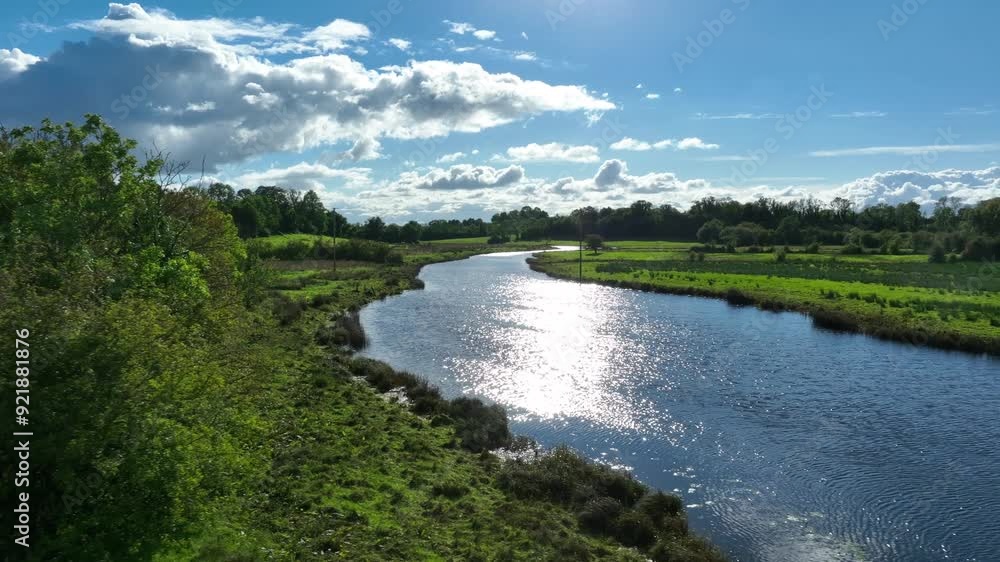 Finn River, County Monaghan, Ireland, September 2022. Drone pulls back over glistening shimmering sparkling water with reeds and shrubs on side at edge of pasture. Finn River, County Monaghan, Ireland, September 2022. Drone pulls back over glistening shimmering sparkling water with reeds and shrubs on side at edge of pasture.