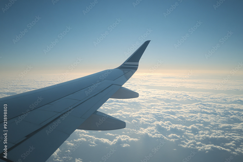 An airplane wing silhouetted against a golden sunset sky with clouds below creating a serene and peaceful scene An airplane wing silhouetted against a golden sunset sky with clouds below creating a serene and peaceful scene