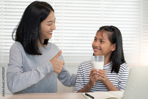 Asian young little girl learn at home. Do homework with kind mother help, encourage for exam. Mom pass on a glass of milk to daughter. Girl happy Homeschool. Mom teach and advice education together..