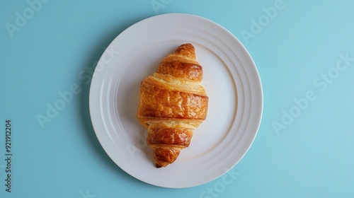 A croissant is placed on a white plate, set against a light blue background. The image showcases a breakfast concept. photo