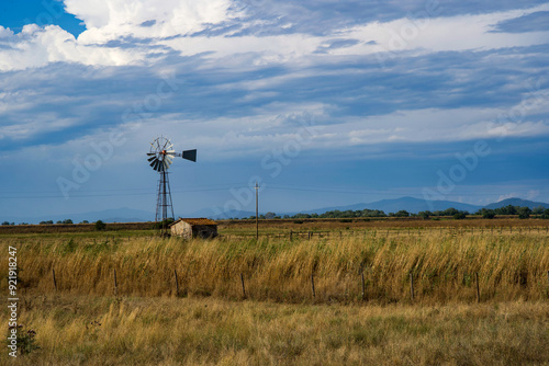 Beautiful landscape with abandoned shack and windmill, dark blue sky before rain. 