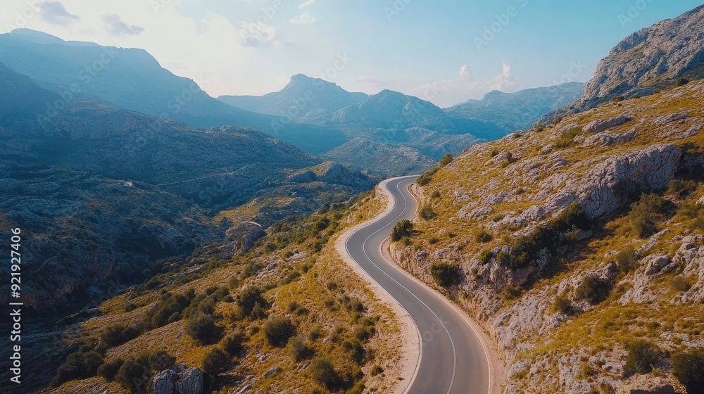 Fototapeta premium Aerial shot of a picturesque road through a mountain pass with clear skies and rocky terrain. Perfect for outdoor adventure themes