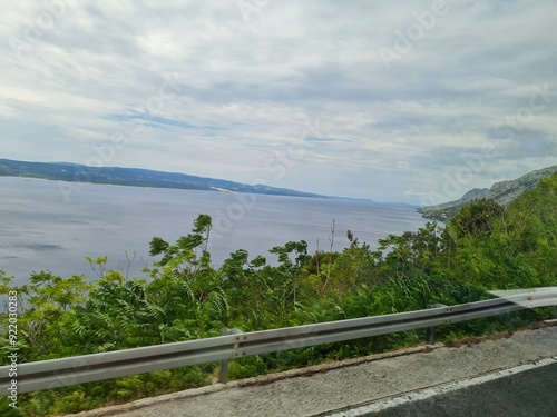 Scenic landscape of mountains and sea on a cloudy summer day. People hurry up to vacation on of beautiful clean place by the Adriatic Sea. View of the coast of rocky island. Curve road in mountain.