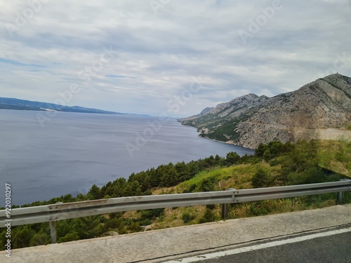 Scenic landscape of  mountains and sea on a cloudy summer day. People hurry up to vacation on of beautiful clean place by the Adriatic Sea. View of the coast of rocky island. Curve road in mountain.
