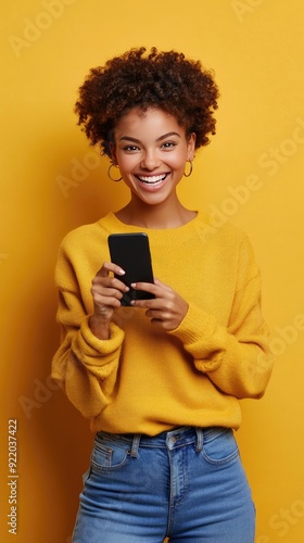 A joyful young black woman is celebrating her achievements as she holds her smartphone, surrounded by a vibrant and sunny yellow backdrop