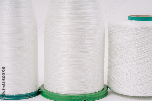 Close-up view of three spools of white fiberglass yarn, showcasing their texture and detail, with a plain white background. photo