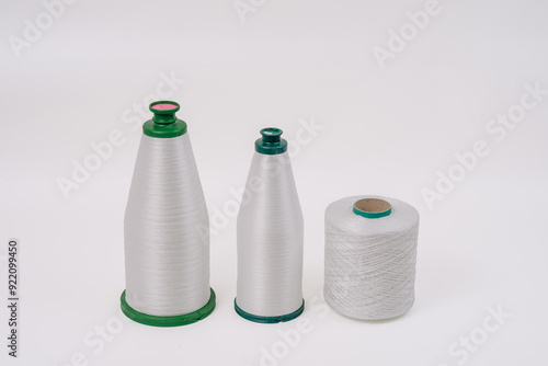 Three spools of white fiberglass yarn, two cone-shaped and one cylindrical, arranged on a plain background, showcasing different textures and shapes. photo