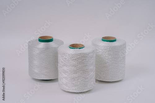 Three spools of white fiberglass yarn are arranged in a row on a neutral background, showcasing their texture and industrial design.